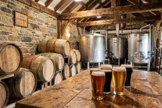 Intérieur authentique d'une brasserie artisanale normande avec tonneaux en bois, verres de bière ambrée et murs en pierre, illustrant le top 10 des brasseries en Normandie
